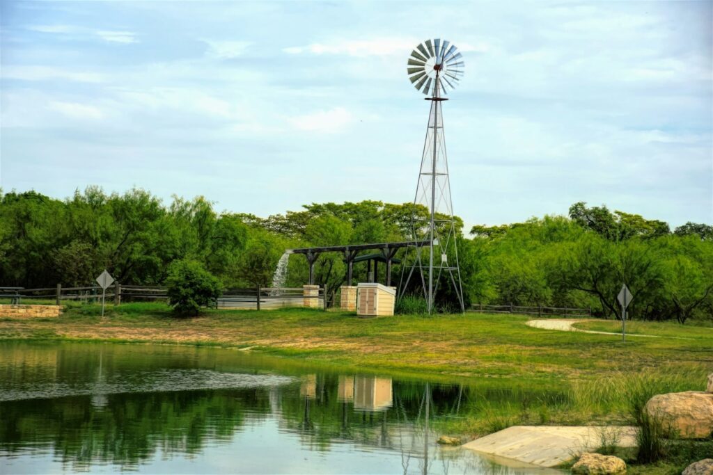 a texas pond in the country with a windmill near the shore.